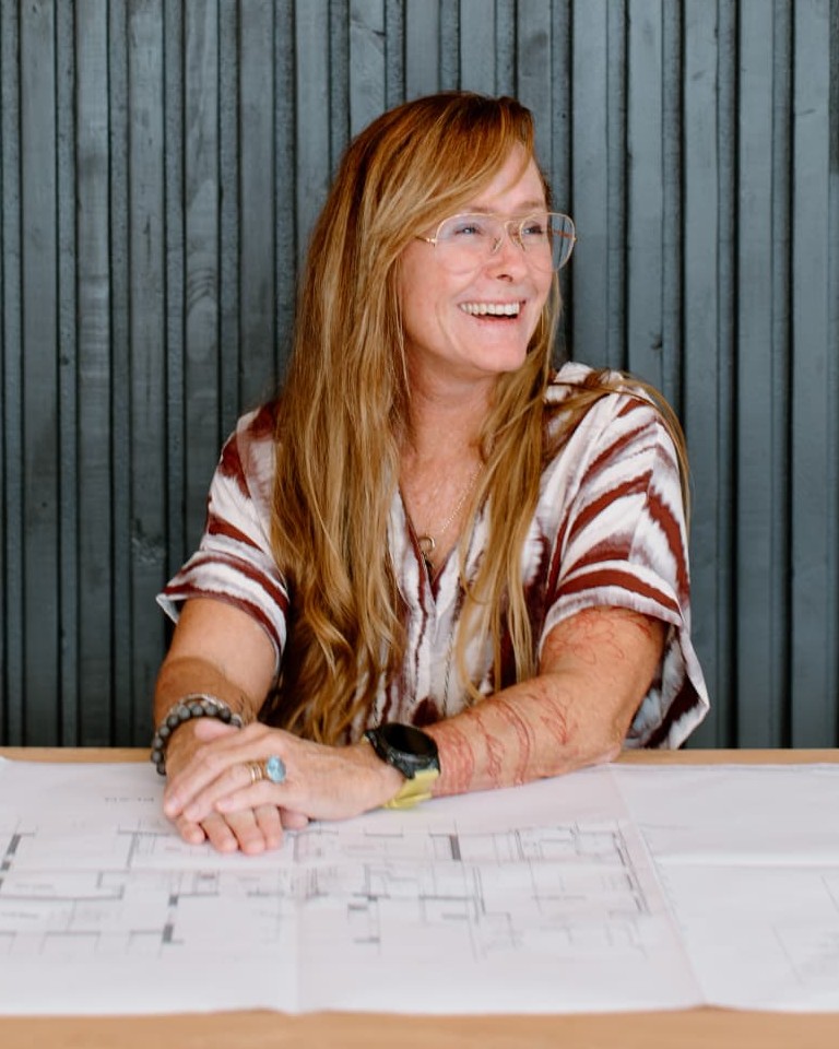 Jennifer Kerr-Marsch seated at her desk with architectural plans, in front of a branded wall